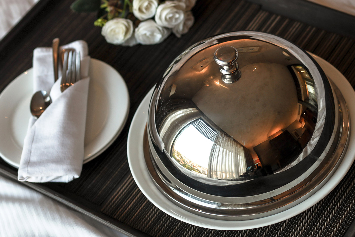 Room service tray with white roses, a food cloche and a plate with cutlery tucked into a serviette